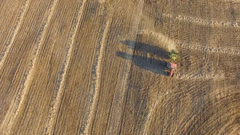 Aerial view of tractor pulling a baling machine across flat farmland at Stock Footage 97145249