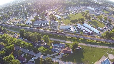 Aerial View of train coming down tracks beside fairgrounds in late afternoon Stock Footage 40366167