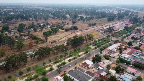 Aerial view of a train moving through a town with buildings and trees under a Stock Footage 307899526