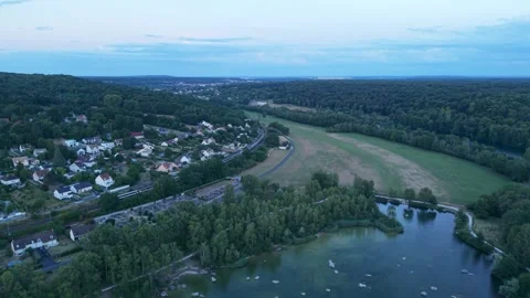 Aerial view of a train passing through a green valley village at dusk, France Video stock 339581005