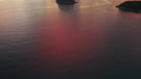 Aerial view of tranquil ocean with island and colorful sunset reflections Stockbeeldmateriaal 337418436