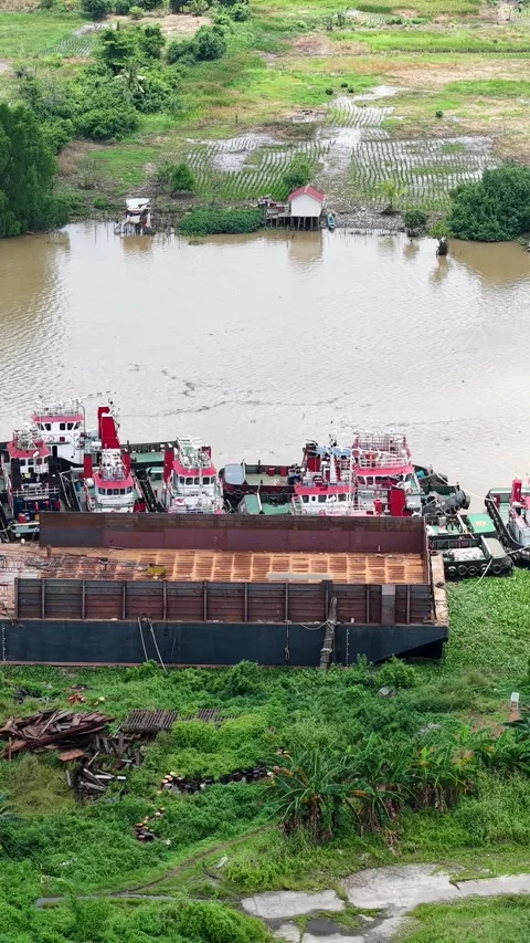 Aerial view of tugboats parked in a row on the riverbank next to barges Stock Footage 335337853