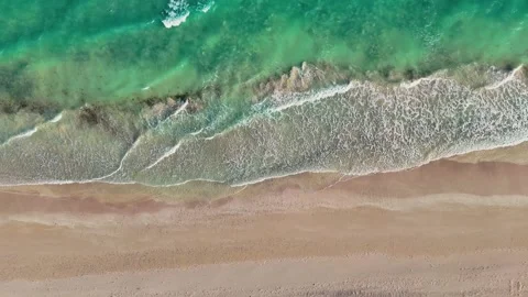 Aerial view of turquoise ocean waves washing onto a sandy beach. Stock Footage 323429491