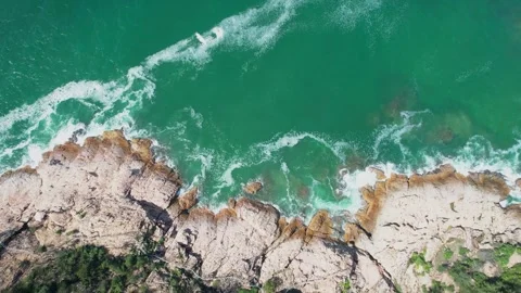 Aerial View of Turquoise Ocean Waves Crashing Against Rugged Rocky Shoreline Stock Footage 342025245
