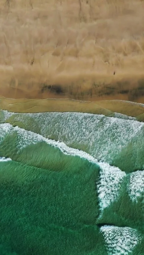 Aerial view of turquoise ocean waves crashing onto a sandy beach shoreline Stock Footage 342573017