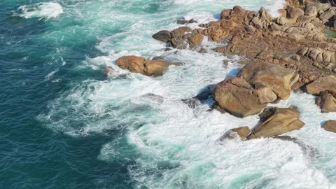 Aerial view of turquoise ocean waves crashing against rugged rocks along the Stock Footage 346691357
