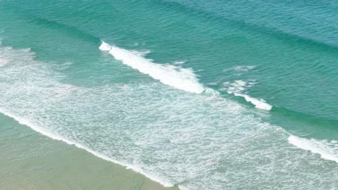 Aerial view of turquoise ocean waves gently rolling onto the sandy shore at Stock Footage 346714154