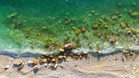 Aerial view of turquoise sea waves gently splashing against pebbles and rocks Stock Footage 336316009
