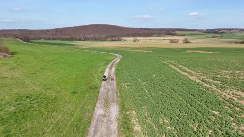 Aerial view of two children riding a quad bike along a dirt path through open Vidéo 332777445
