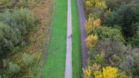 Aerial view of two cyclists riding along path surrounded by autumn foliage Stock Footage 320114850