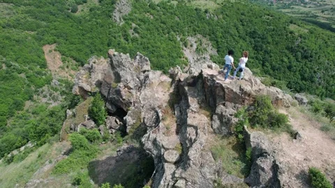 Aerial view of two hikers explorers atop of rugged mountain peak surrounded b Stock Footage 320640023