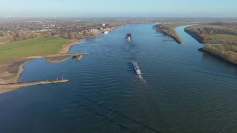 Aerial view of two large cargo ships navigating a wide river, with grassy banks Видео 329811378