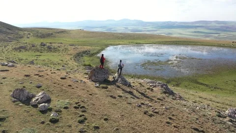 Aerial view of two people looking around on the rock by the lake Stock Footage 293982940