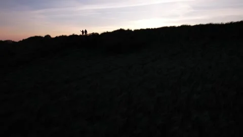 Aerial View of Two People Silhouetted on Hillside at Sunset Stock Footage 343520932