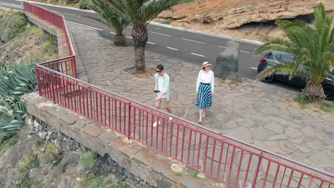 Aerial view of two people standing on the edge of a cliff on an island in the Видео 108688604