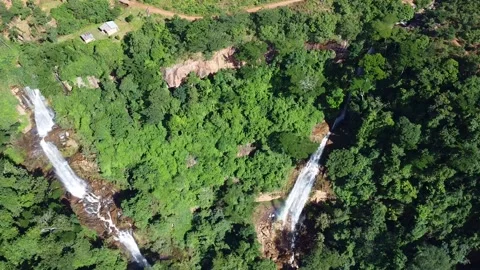 Aerial view of two waterfalls cascading through a dense green forest with a dirt Stock Footage 316947428