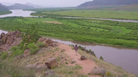 Aerial view of a valley between mountains and a flowing river. A woman walks Stock Footage 323432363