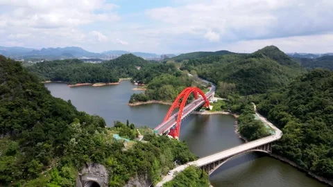 Aerial view of a vibrant red arch bridge crossing a scenic mountain lake Video stock 342303362