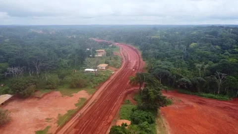 Aerial view of a vibrant red road cutting through dense, lush green forest. Stock Footage 315256053