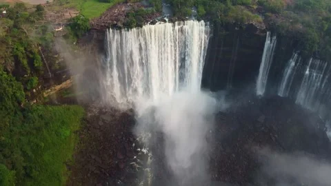 Aerial view of a waterfall cascading over rocks with lush greenery and mist in Stock Footage 307890667