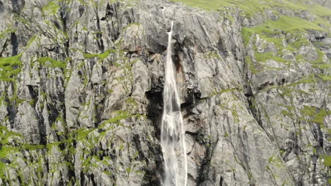 Aerial view waterfall flows down from the mountains, forming a stream and fog Stock Footage 147375799