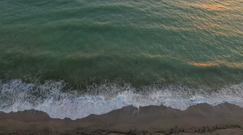 Aerial view waves break on white sand beach at sunset, land meets sea Stock Footage 68916824