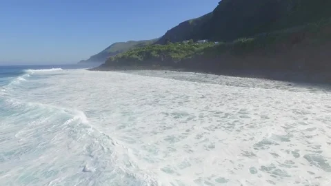 Aerial view of the waves breaking on the shore of the rocky beach with a blue Stock Footage 148793798