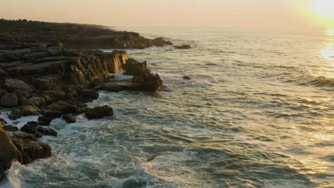 Aerial view of waves breaking at sunset on the rocks of the rugged, rocky beach Stock Footage 153758697