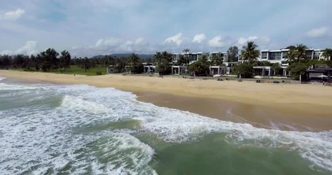Aerial View of Waves Crashing on a Sandy Beach with Coastal Villas Stock Footage 300844151