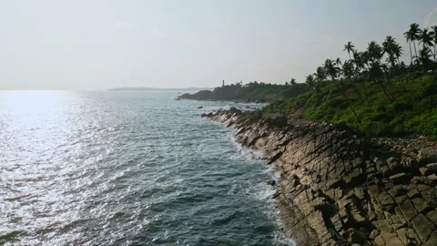Aerial view of waves hitting rocky shore near hilltop lighthouse. Scenic Stock Footage 264885326