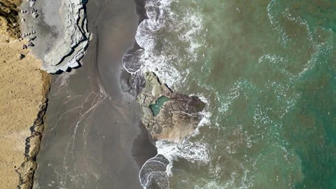 Aerial view of waves washing over a rocky black sand beach Stock Footage 345197944