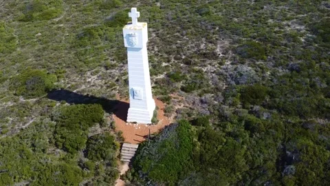 Aerial view of a white tower structure surrounded by green vegetation and a road Stock Footage 308978472