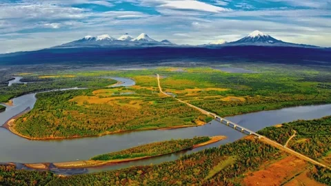 Aerial view of wide river and long bridge near snow covered volcanoes in wild Stock Footage 345484123
