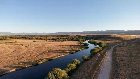An aerial view of a wide river running parallel to a road through flat golden Stock Footage 328524973