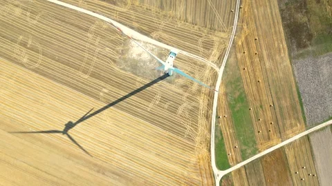 Aerial view of a wind turbine casting a long shadow over harvested fields in Stock Footage 287494863
