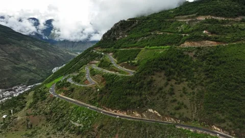 Aerial view of winding cliffside highway on layered green mountain ridge in Stock Footage 336698768