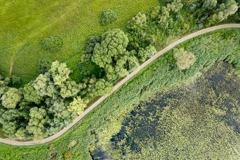 Aerial View of a Winding Path Between a Lake and Green Field Stock Photos