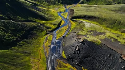 Aerial view of a winding river cutting through a green moss-covered volcanic Stock Footage 331196016
