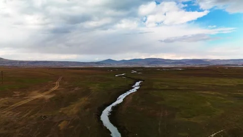 Aerial view of a winding river flowing through a vast green plain under a cloudy Stock Footage 332723384