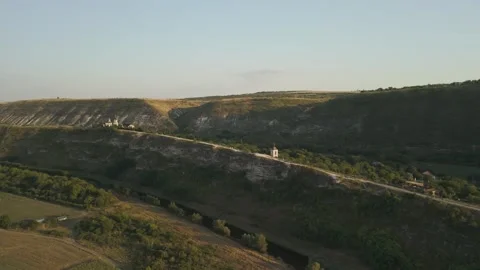 Aerial view of a winding river flowing through lush green fields and rocky hills Stock Footage 332725620
