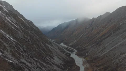 Aerial view of winding river through rugged mountain valley, camera pans Vídeos de archivo 320396140