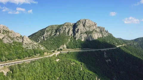 Aerial view of a winding road passing through lush green mountains and rocky Stock Footage 346664604
