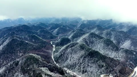 Aerial view of a winding road through a snowy mountain forest in winter Stock Footage 342304316