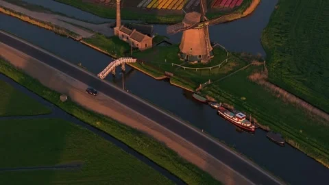 Aerial view of windmill and blooming tulips lining a sunset-lit canal, Holland Stock Footage 313365201