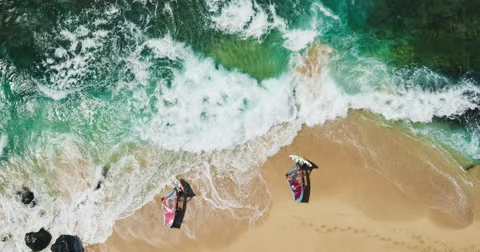 Aerial view of windsurfers launching into blue ocean from white sand beach Stock Footage 63540703