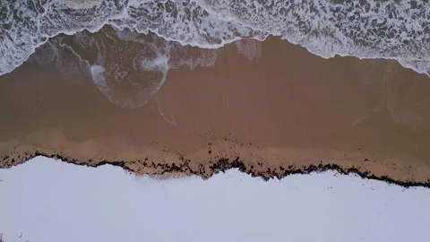 Aerial view of a winter beach where ocean waves meet the sandy shore and snow. A Stock Footage 302442216