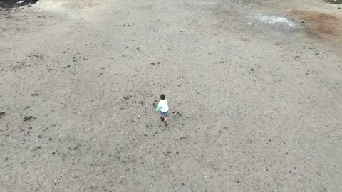Aerial view of young boy running across rocky terrain with patches of green Stockbeeldmateriaal 341123637