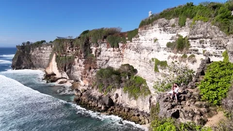 Aerial view of young lady is seating on a cliff Uluwatu, in in Bali, Indonesia Stock Footage 315752048