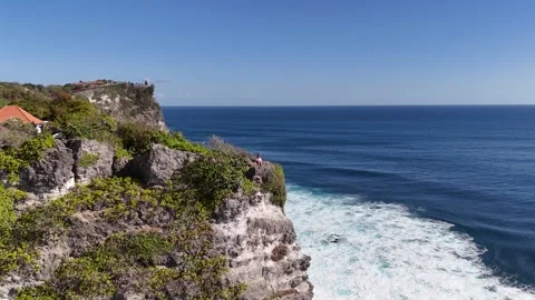 Aerial view of young lady is seating on a cliff Uluwatu, in in Bali, Indonesia Stock Footage 315752164