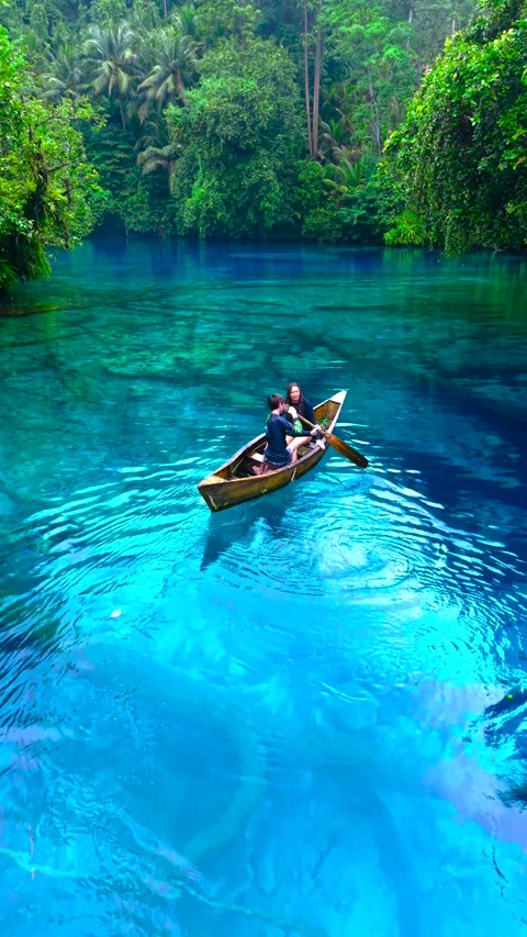 Aerial view of a young man and a young woman paddling a wooden canoe on clear Stock Footage 346055008
